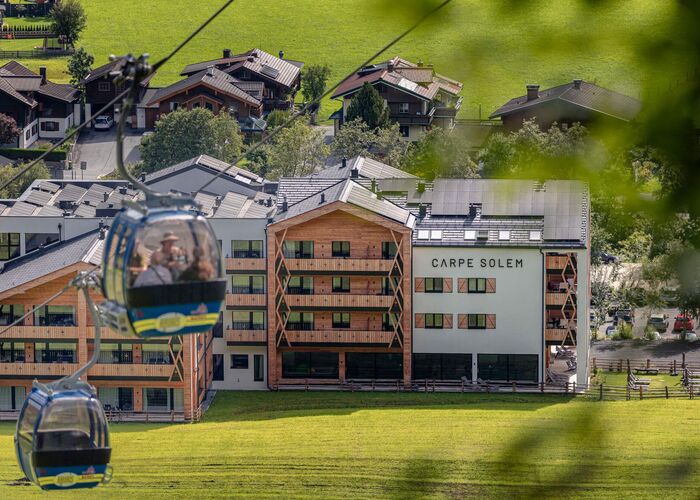 Außenansicht des Carpe Solem Rauris im Sommer mit Gondel und direkter Lage an der Bergbahn im Raurisertal.