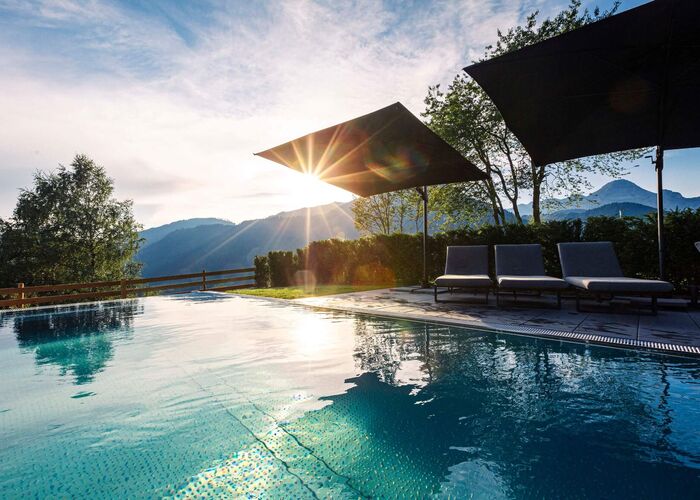 Außenpool im Hideaway Dachstein West mit Liegen, Sonnenschirmen und Blick auf die Berglandschaft bei tief stehender Sonne.