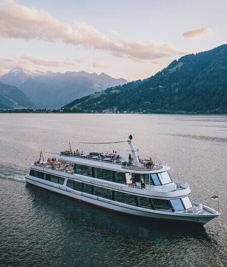 Schiff MS Schmitten fährt am Zeller See, umgeben von Bergen und Gletscher.