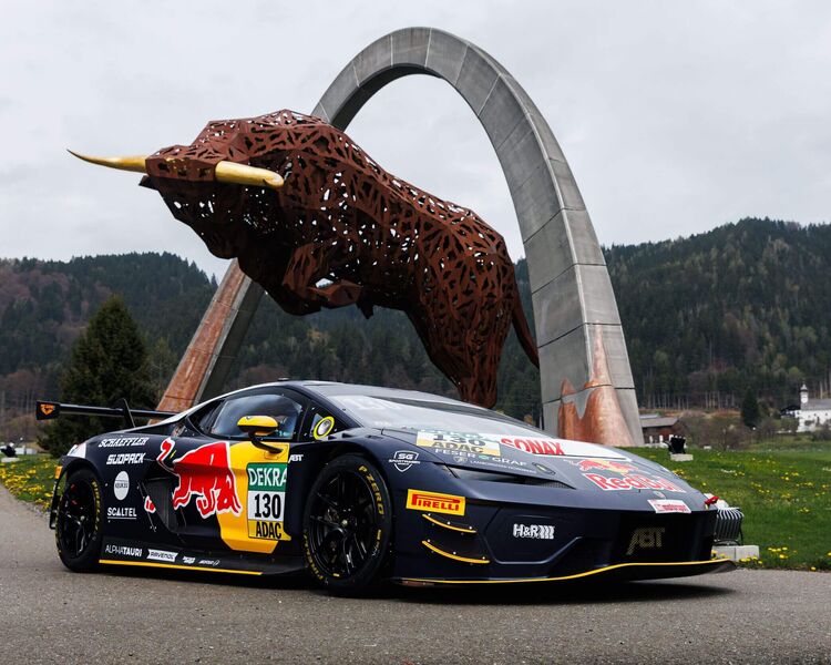 Ein Rennwagen mit Red Bull-Design steht unter einer beeindruckenden Stier-Skulptur in einer malerischen Landschaft.