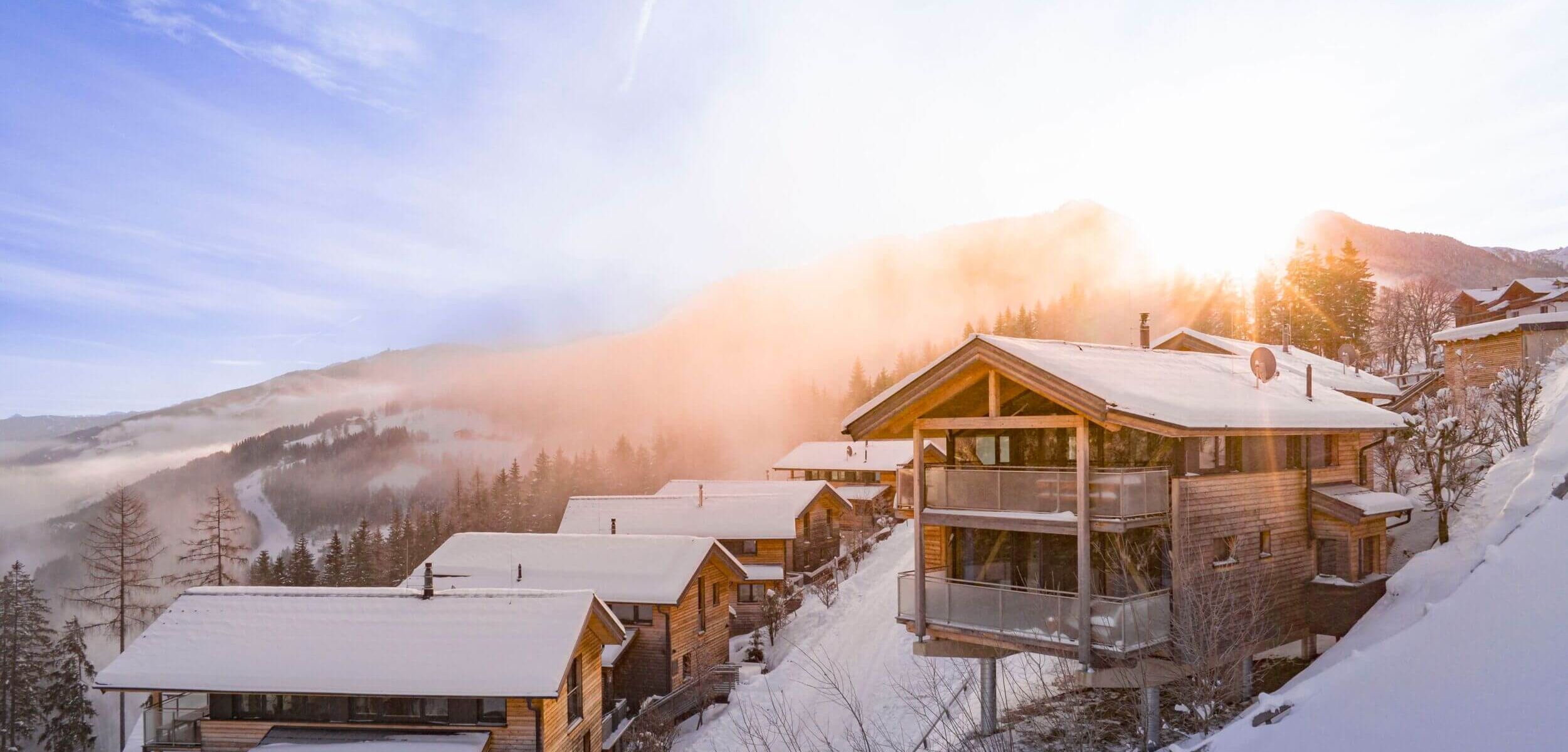 Ferienhäuser und Chalets in winterlich verschneiter Landschaft und Sonnenaufgang