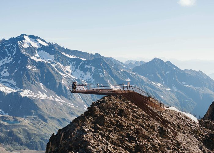 Gipfel der Tiroler Bergplattform im Sommer mit zwei Personen darauf und Bergen im Hintergrund