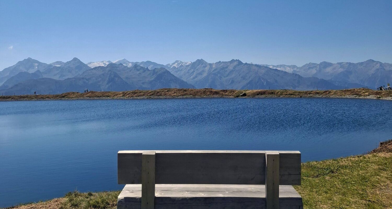 Eine ruhige Bank am Speicherteich bietet einen atemberaubenden Blick auf die Berge unter klarem, blauem Himmel.