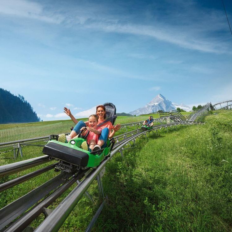 A mother and child enjoy a thrilling ride on the Maisiflitzer coaster in Kaprun, surrounded by mountains.