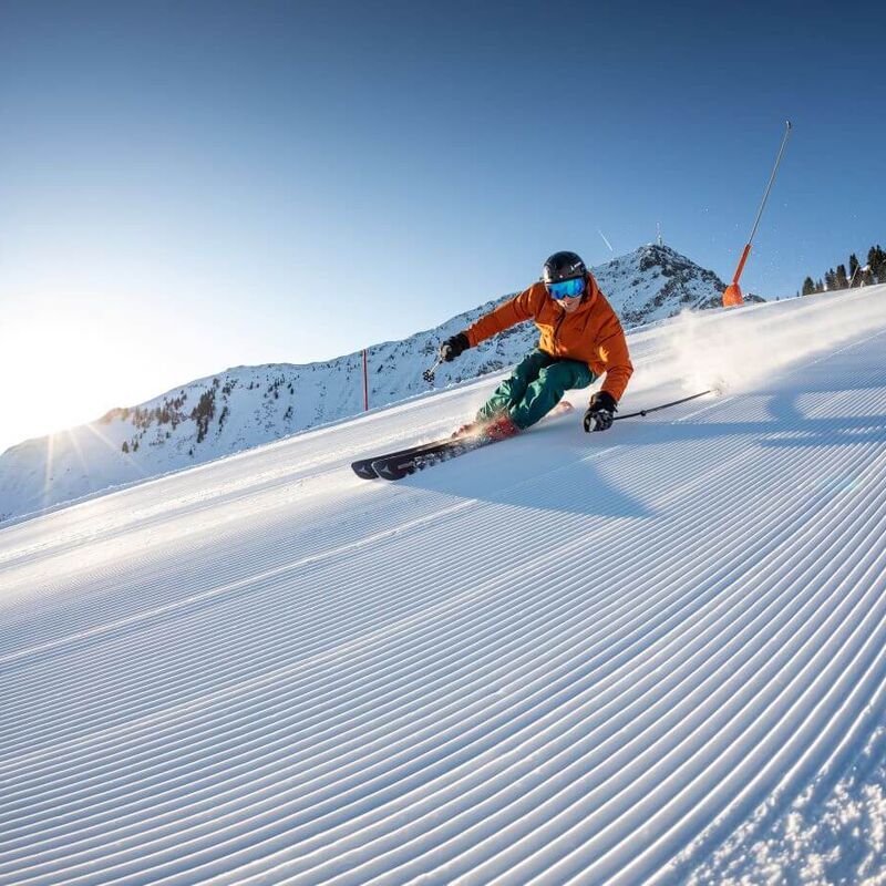 Skifahrer beim Carving-Schwung auf der "schneesicheren Seite des Kitzbüheler Horns": St. Johann in Tirol