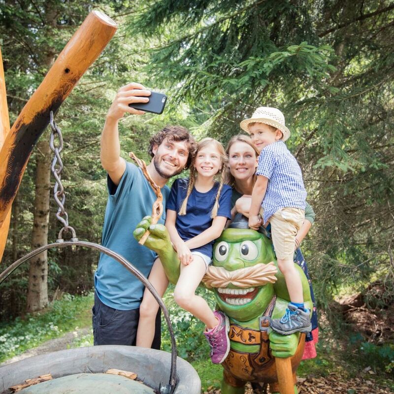 A family takes a selfie with a friendly green statue in the scenic Tiroler Zugspitze forest.