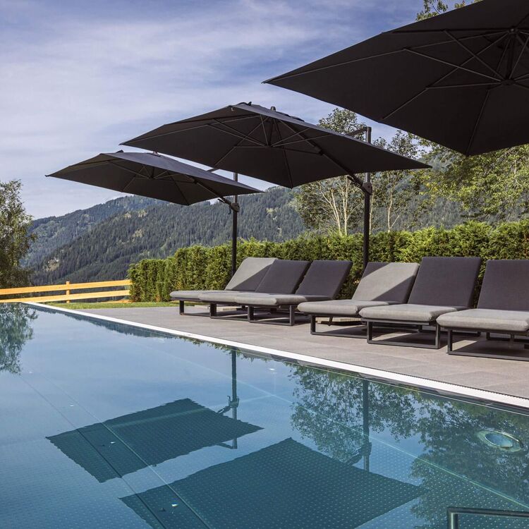Moderner Infinitypool mit extrabreiten Sonnenliegen, weich gepolsterten Auflagen und großen Sonnenschirmen sowie traumhaftem Ausblick auf die grüne Berglandschaft im Salzburger Land.