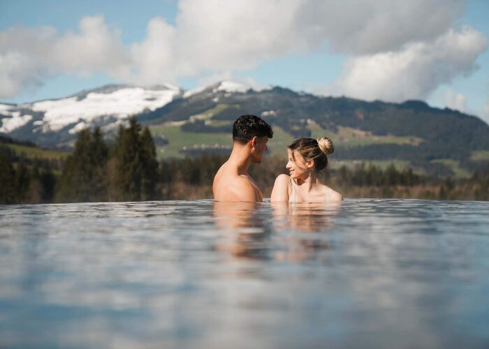 Ein Paar entspannt im Infinity-Pool mit Blick auf die schneebedeckten Alpen.