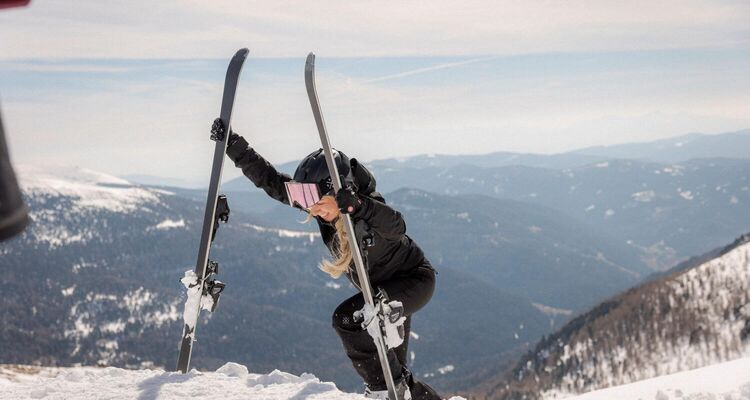 Eine Frau mit Skiern kämpft sich durch den Schnee auf einem Berg in der schönen Winterlandschaft.