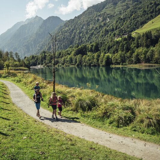 A family with two children walks around the idyllic Klammsee lake surrounded by high mountains.