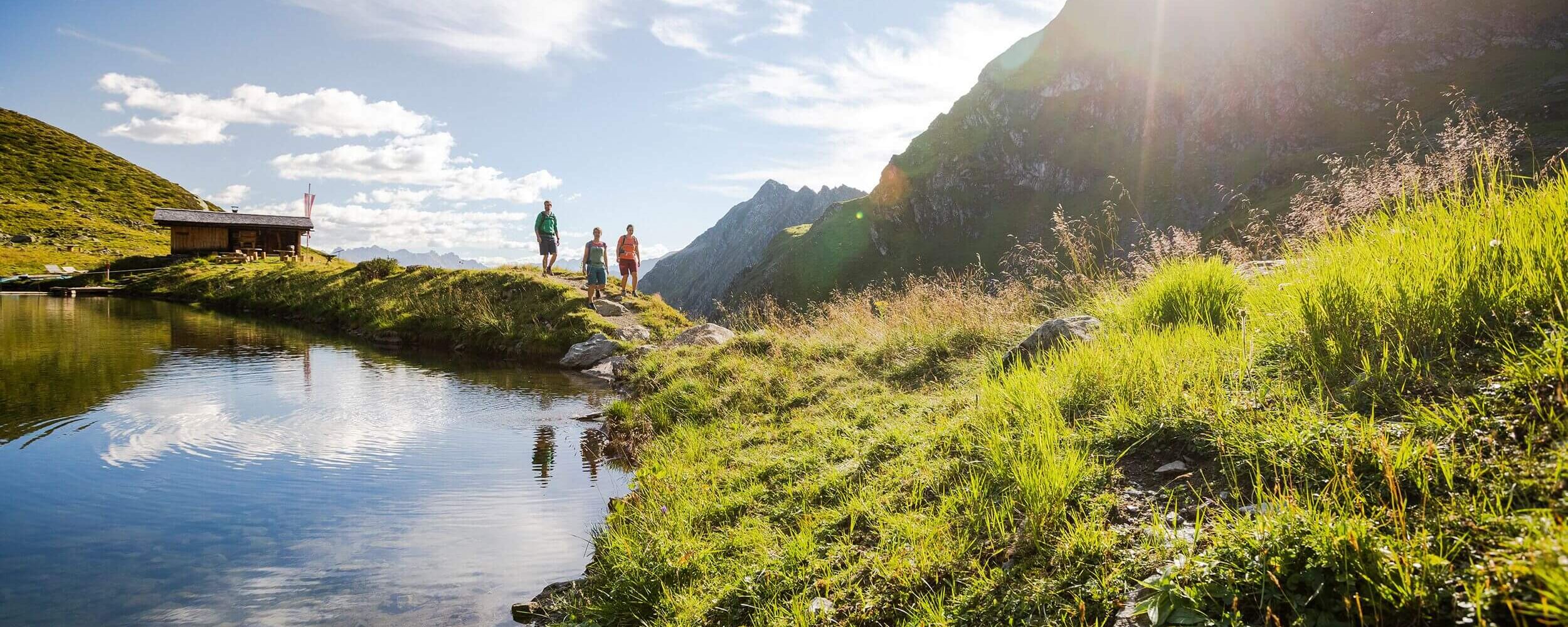 Gezin wandelt langs een bergmeer met een traditionele Tiroolse hut en een alpenberglandschap op de achtergrond