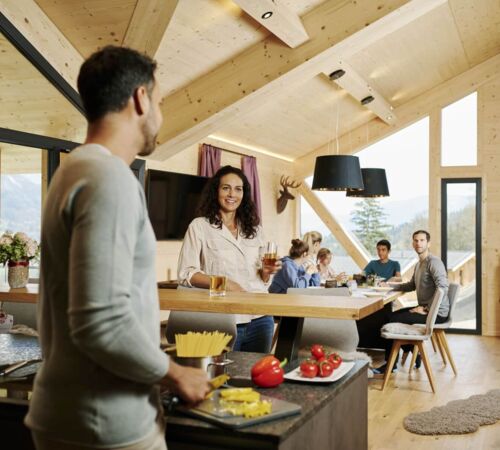 Familie kocht im Ferienhaus, Kinder spielen am Esstisch