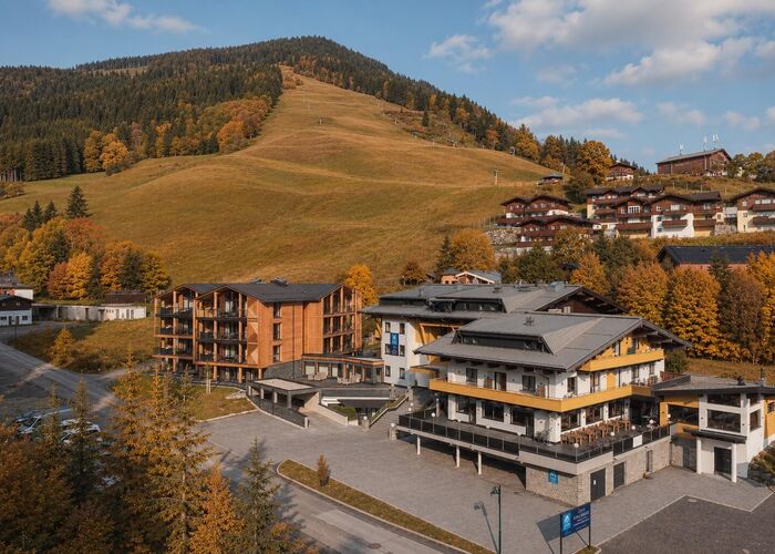 Herbstliche Aussicht auf die Saalbach Suites mit bunten Bäumen und sanften Hügeln im Hintergrund.