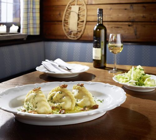 Gedeckter Holztisch mit Kärntner Kasnudeln, grünem Blattsalat und einer Flasche Weißwein