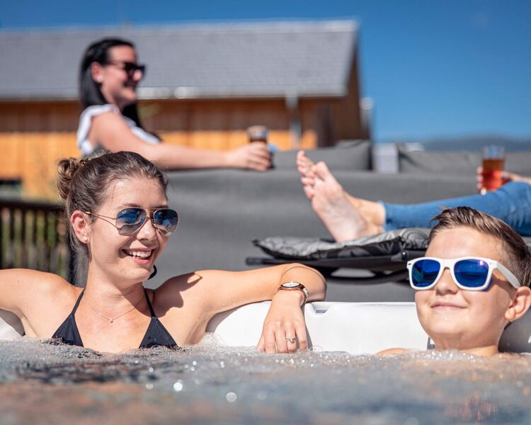 Eine Frau und ein Junge entspannen im Whirlpool, während eine weitere Person im Hintergrund sitzt und ein Getränk genießt.