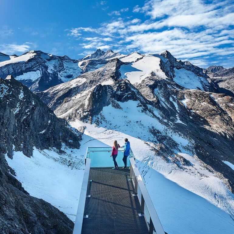 A couple looks out from a panorama platform at the Großglockner and other 3,000-metre peaks of the Hohe Tauern.