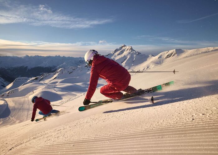 2 Skifahrer carven eine lange Abfahrt auf der frisch präparierten Piste im Skigebiet Silvretta Montafon hinunter.