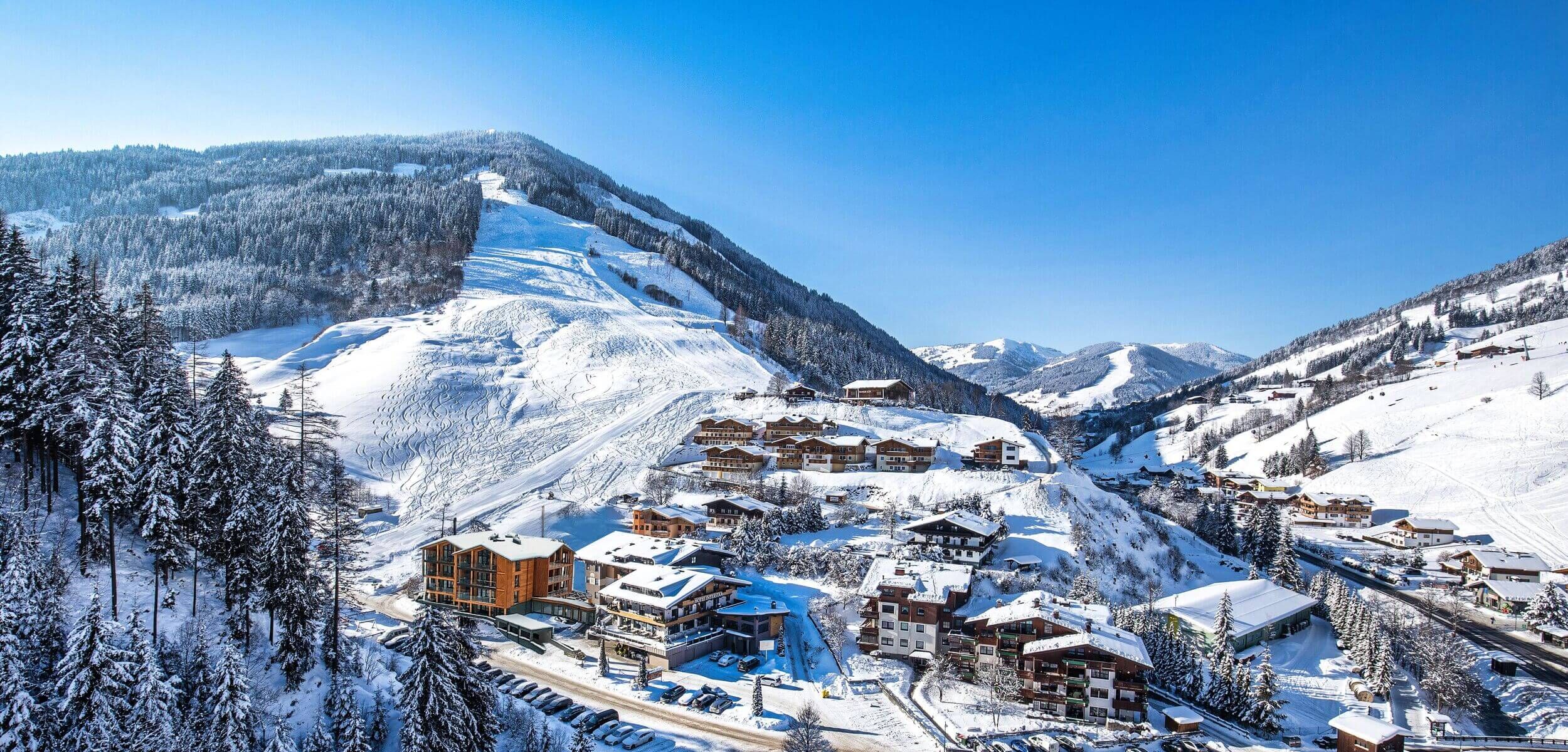 Ferienwohnungen und Häuser an einer Skipiste in Österreich mit viel Schnee und traumhaft blauem Himmel