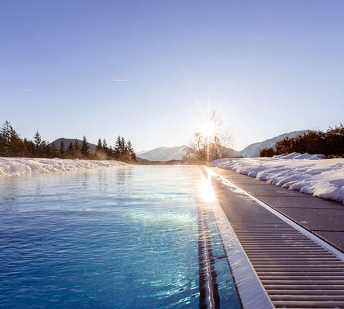 Infinitypool im Winter mit verschneiter Terrasse und Blick auf die umliegenden Wälder und Berge.