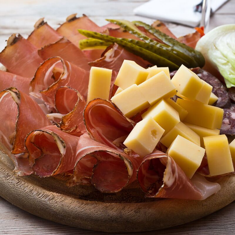 Wooden board with cured ham, cubed cheese, salami and pickles