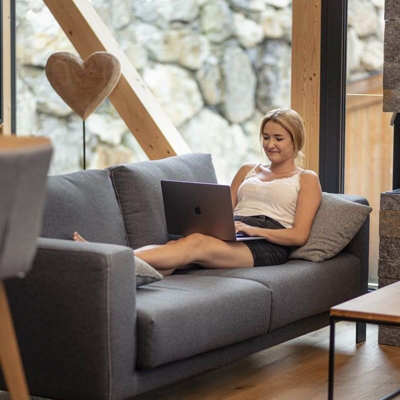 Eine junge Frau sitzt mit ihrem Laptop am Sofa.