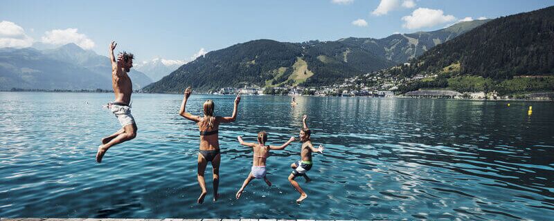 Familie springt in den Zeller See, im Hintergrund das Kitzsteinhorn und die Stadt Zell am See.