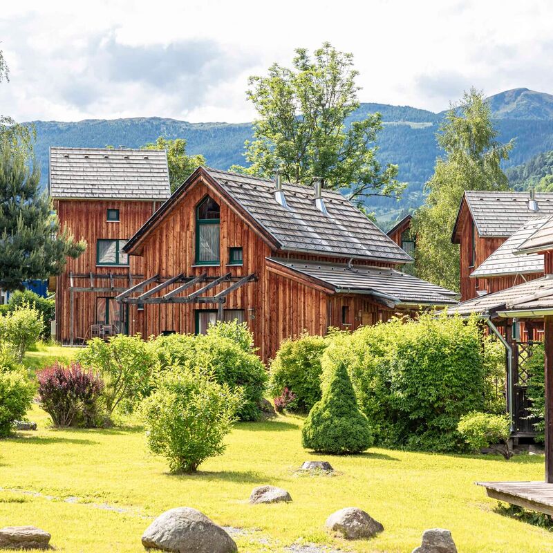 Chalets umgeben von grünem Garten und Bergen im Hintergrund.