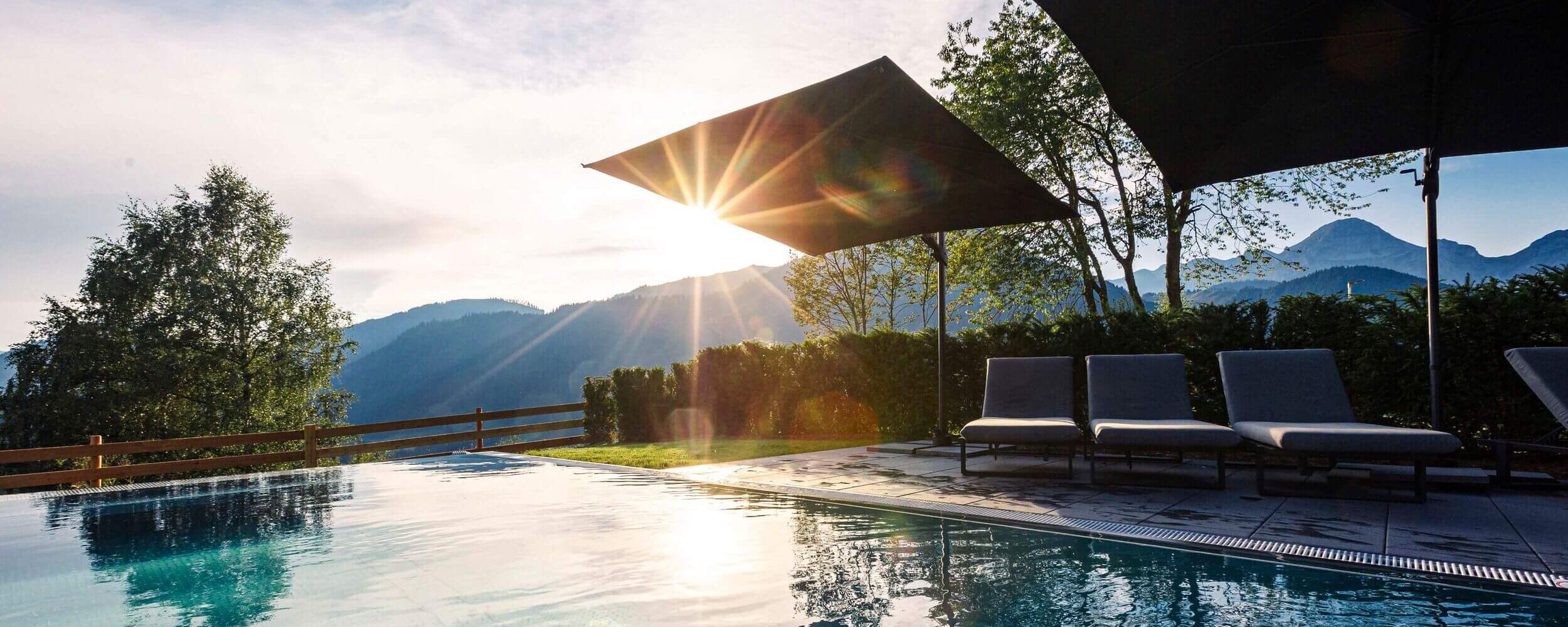 Außenpool im Hideaway Dachstein West mit Liegen, Sonnenschirmen und Blick auf die Berglandschaft bei tief stehender Sonne.