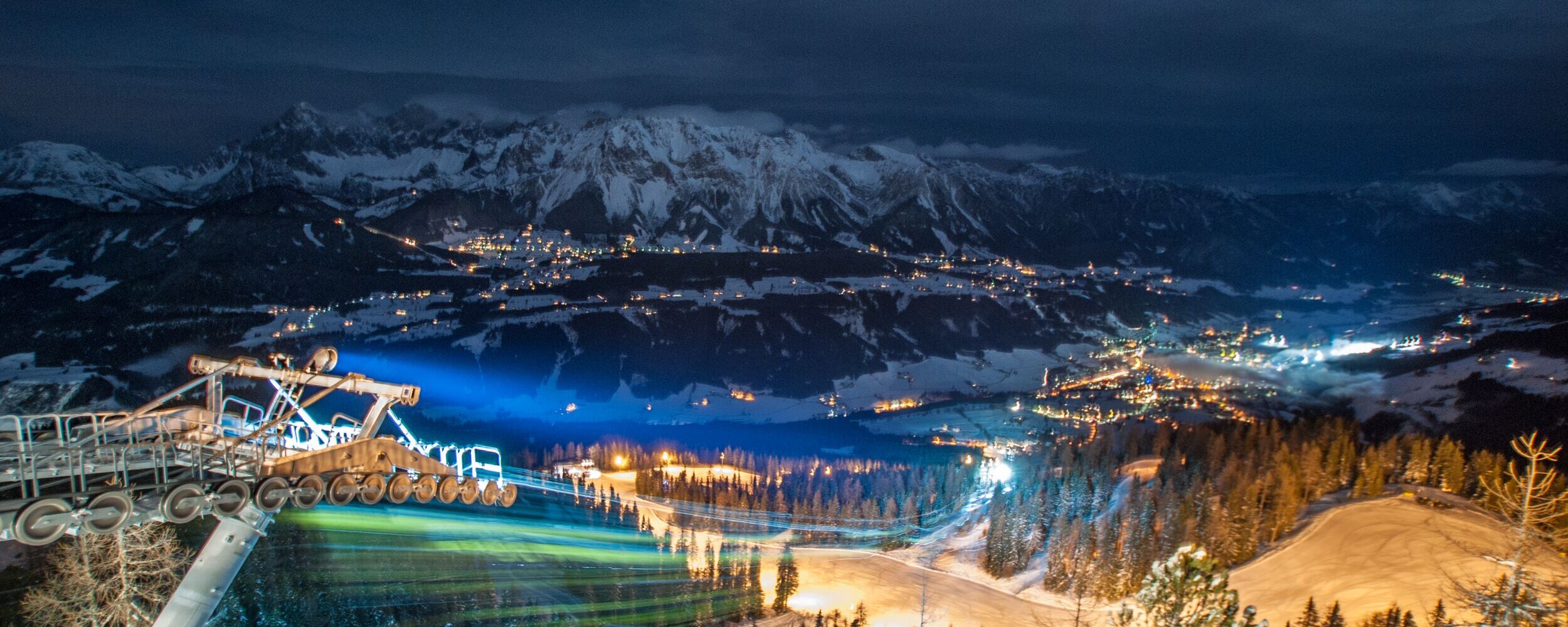 Blick auf die beleuchtete Winterlandschaft von Hochwurzen bei Nacht, umgeben von schneebedeckten Bergen.