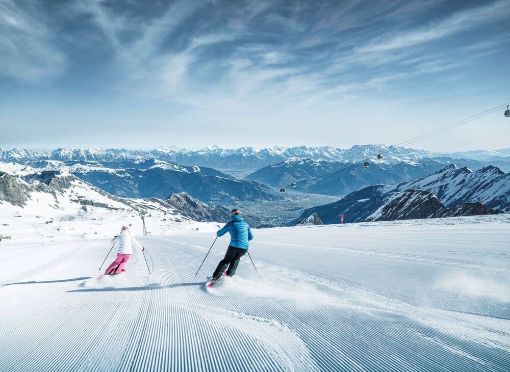 2 Skifahrer am Gletscher, im frühlingshaften Tal sieht man den Zeller See.