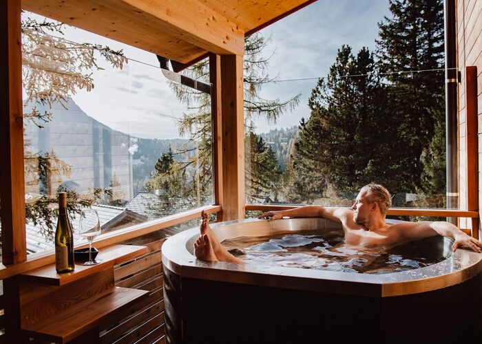 Guest relaxing in the private hot tub of a Naturchalet on the Turracher Höhe with views of the snowy forest and mountain landscape.