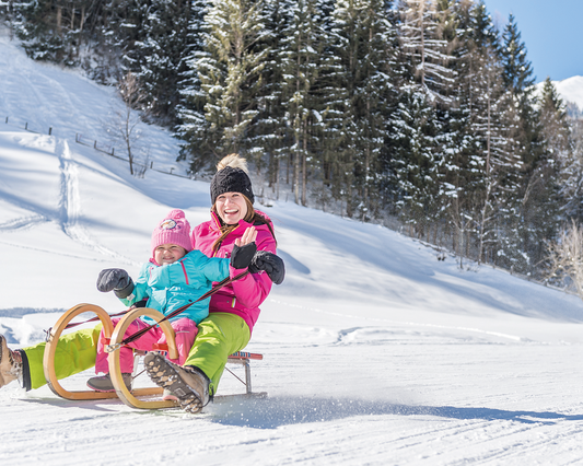 Mutter mit kleinem Kind sitzt auf einem Schlitten auf einer flachen Rodelbahn