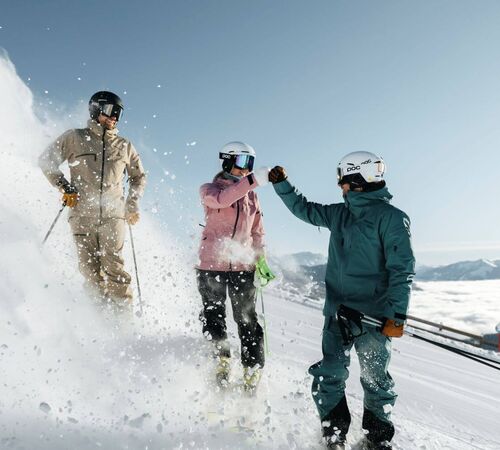 3 skier friends stand on the piste and give each other a high five.