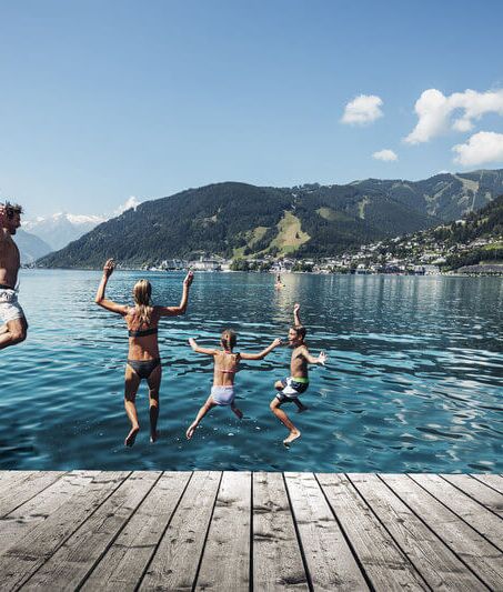 Familie springt in den Zeller See, im Hintergrund das Kitzsteinhorn und die Stadt Zell am See.