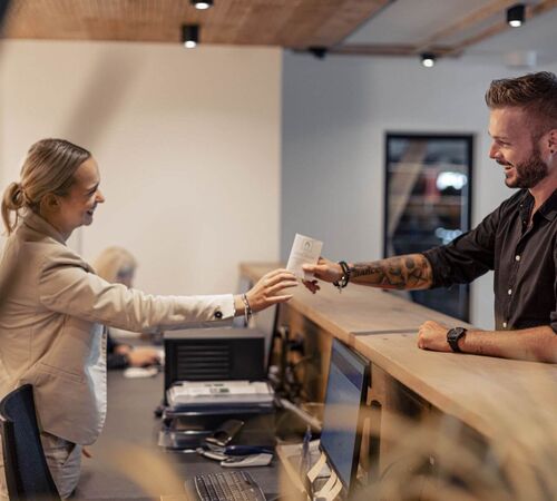 A receptionist hands her guest a key card.