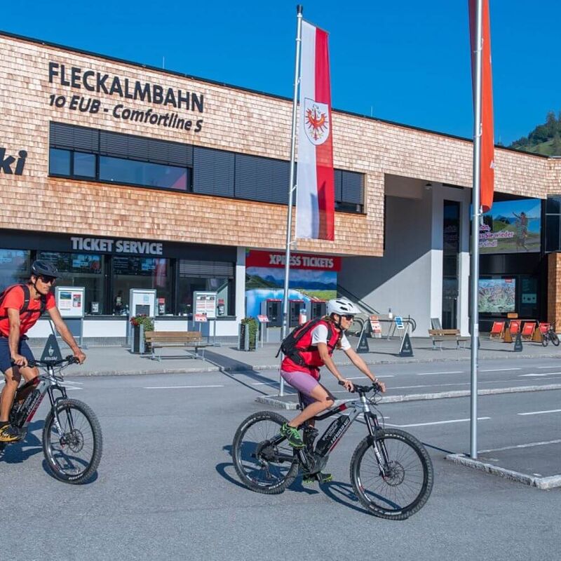 2 e-bikers cycle to the valley station of a summer mountain railway.