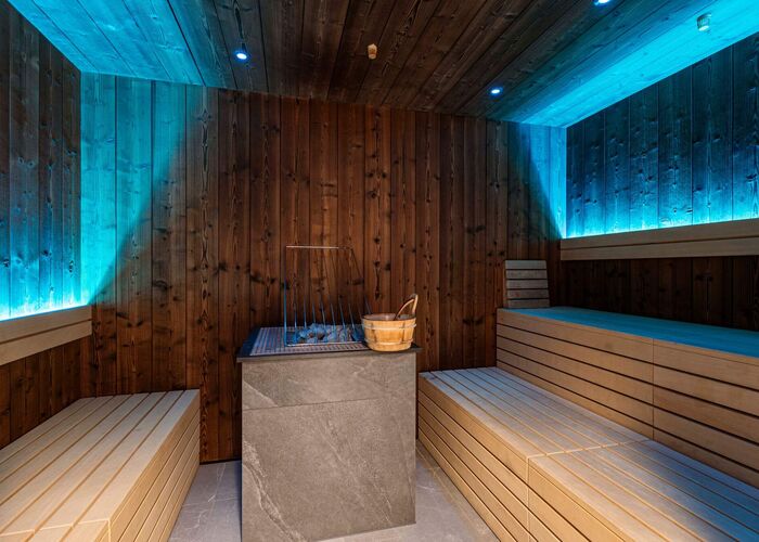 Sauna with cosy wooden benches, stone sauna heater and relaxing lighting