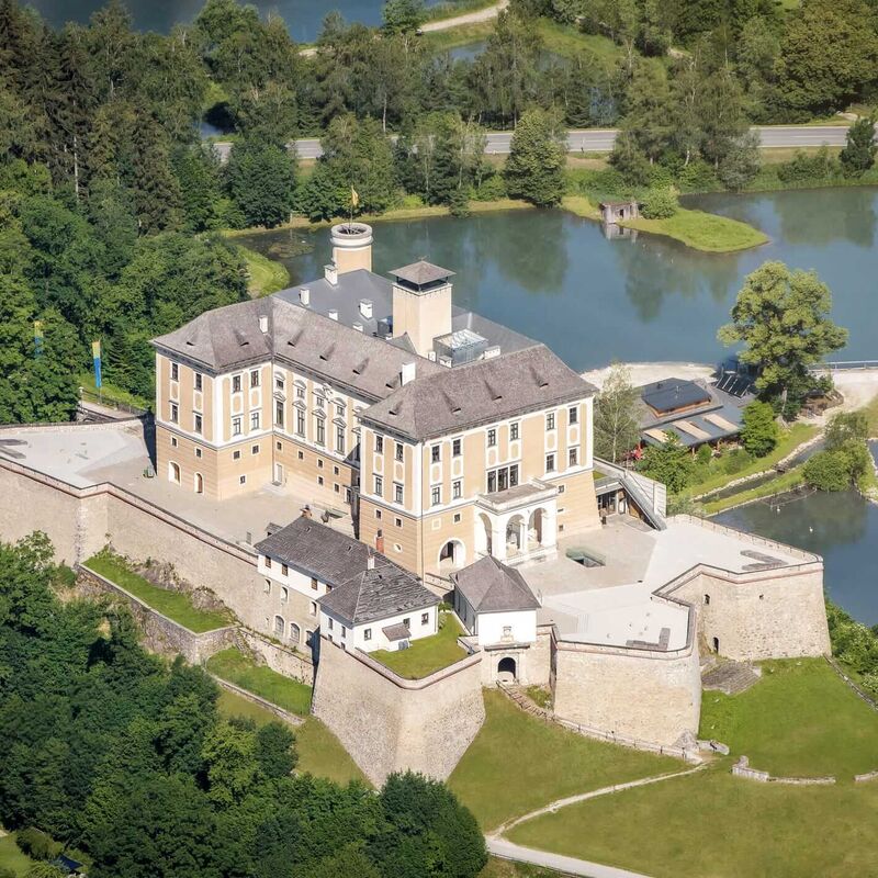 Luftaufnahme von Schloss Trautenfels mit historischem Schlossgebäude, Teichen und grüner Landschaft