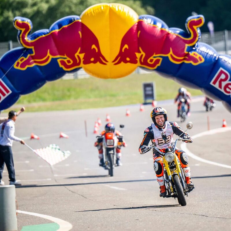 Ein Motorradfahrer überquert unter einem Red Bull-Bogen die Ziellinie bei einem Rennen.
