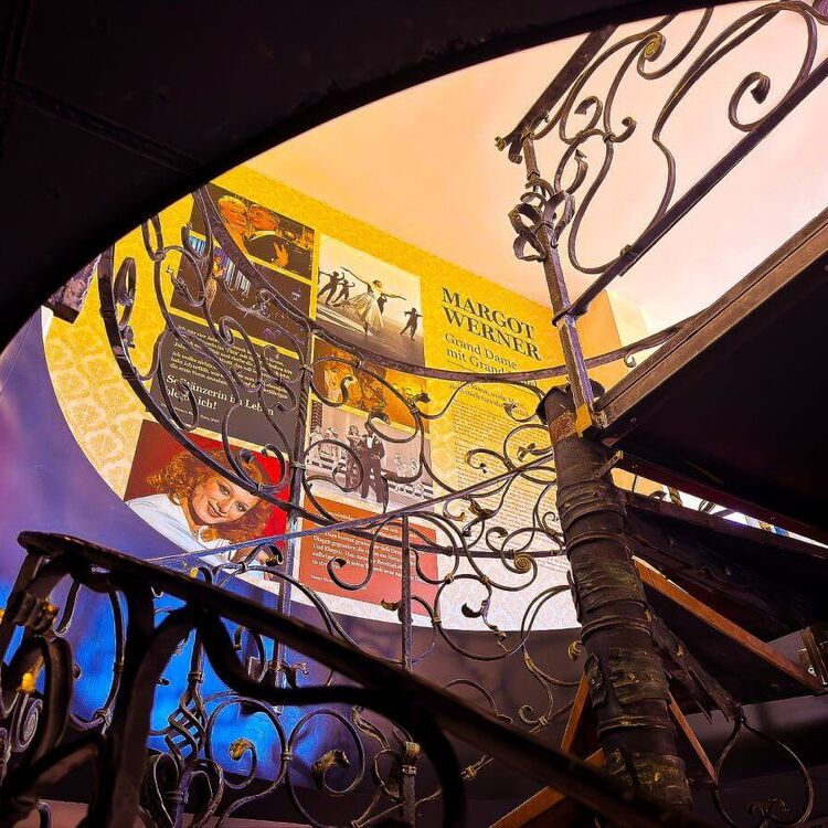View from below of the wrought-iron spiral staircase with a photo wall dedicated to Margot Werner in the "Room of the Stars"