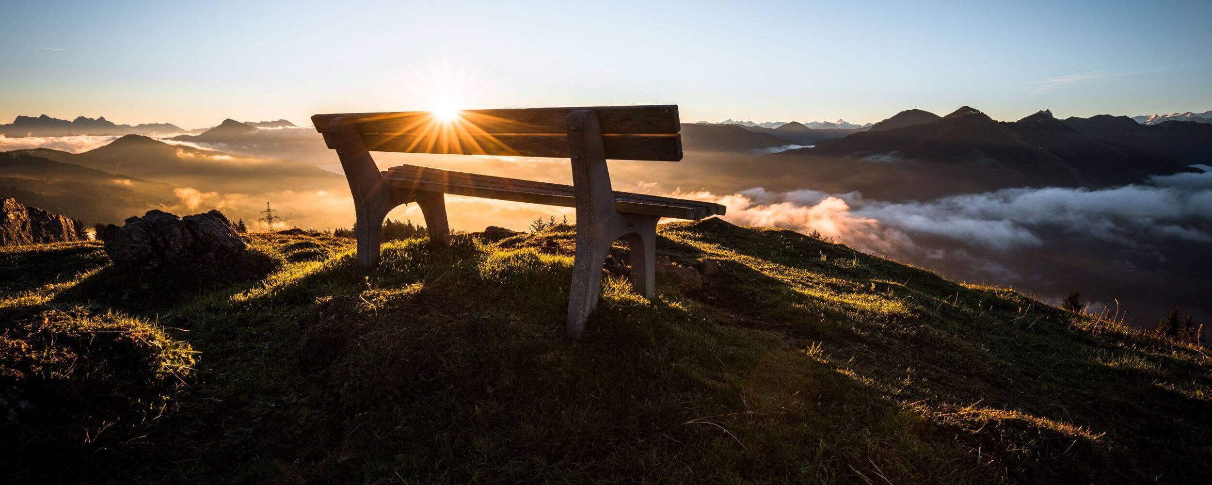 A wooden bench overlooks misty mountains at sunrise in Tirol, capturing a serene autumn morning.