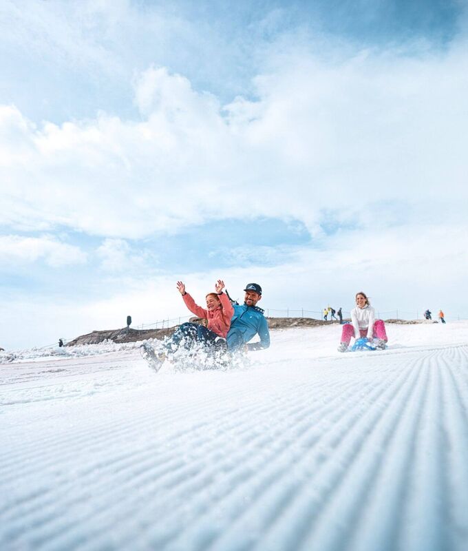 Familie rutscht im Sommer mit Bobs über ein präpariertes Schneefeld am Kitzsteinhorn Gletscher.