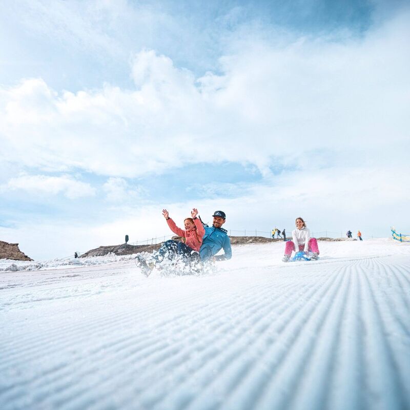 Familie rutscht im Sommer mit Bobs über ein präpariertes Schneefeld am Kitzsteinhorn Gletscher.