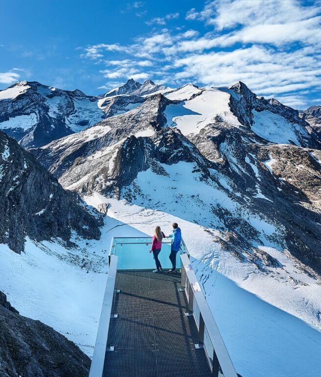 Pärchen blickt von einer Panoramaplattform auf den Großglockner und weitere 3.000er der Hohen Tauern.