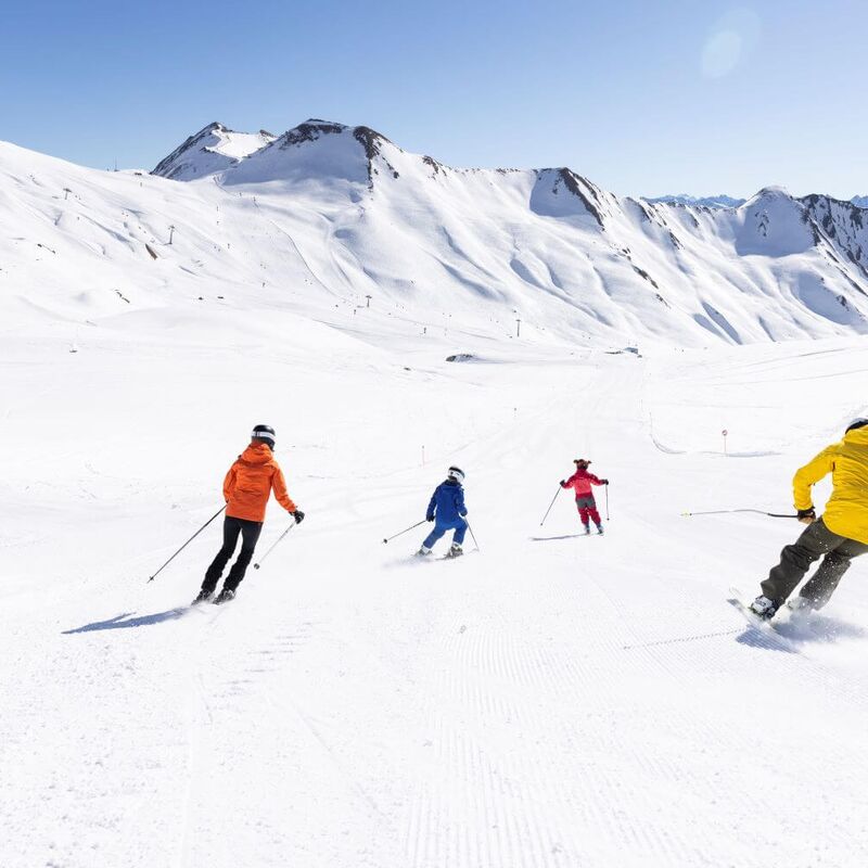 Eltern mit Kindern beim Skifahren auf einer breiten Piste