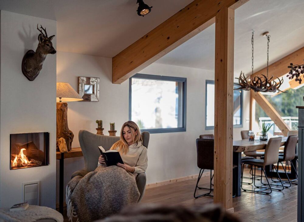 A woman sits with a book in front of the fireplace in her holiday home.