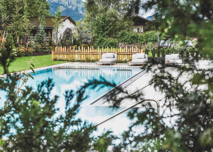 Ein beheizter Außenpool umgeben von grünen Pflanzen und bequemen Liegen in einer einladenden Gartenlandschaft.