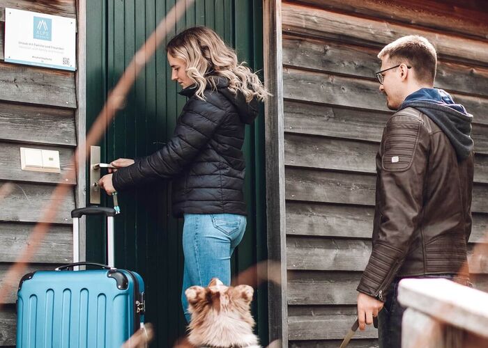 Paar mit Hund und Koffer beim Betreten eines Ferienhauses im Alpendorf Dachstein West