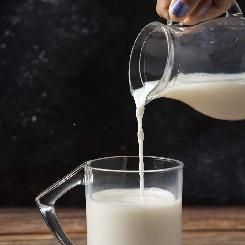 Frau gießt Milch in ein Glas zur Vorbereitung des Kaiserschmarrn Teigs