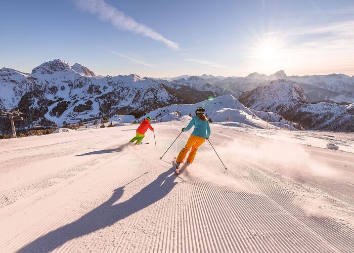 2 Skifahrer genießen Sonnenskilauf auf perfekten Pisten am Nassfeld/Kärnten mit Blick auf den Gartnerkofel.